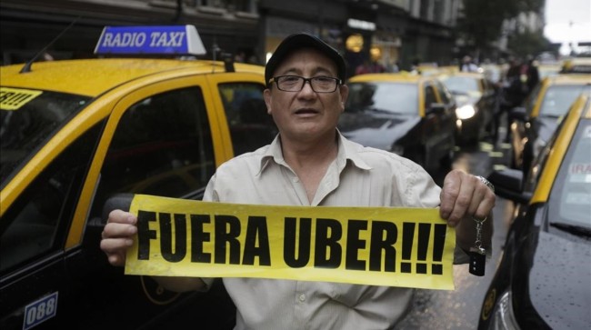 A taxi driver holds a sign that reads in Spanish  Get out Uber  as cabbies block an avenue to protest Uber in downtown Buenos Aires  Argentina  Friday  April 15  2016  Taxi drivers paralyzed parts of Buenos Aires during rush hour against Uber launching its service in Argentina s capital city in defiance of local authorities   AP Photo Victor R  Caivano